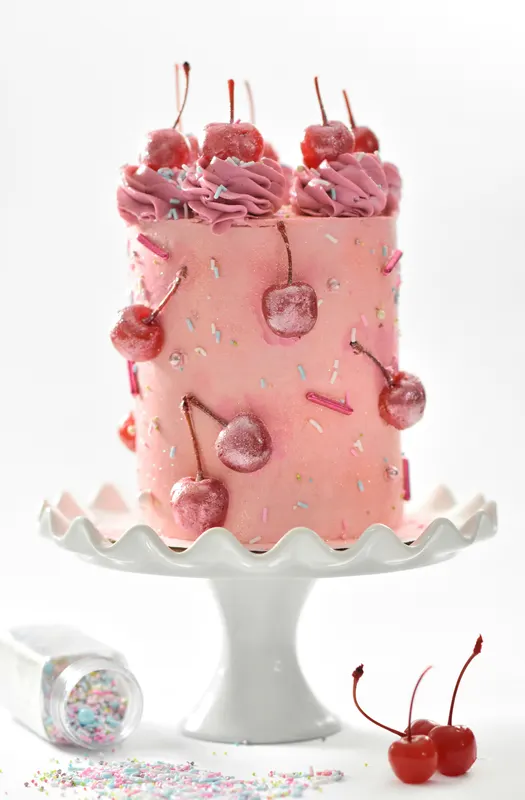 Tall pink cake topped with buttercream and cherries