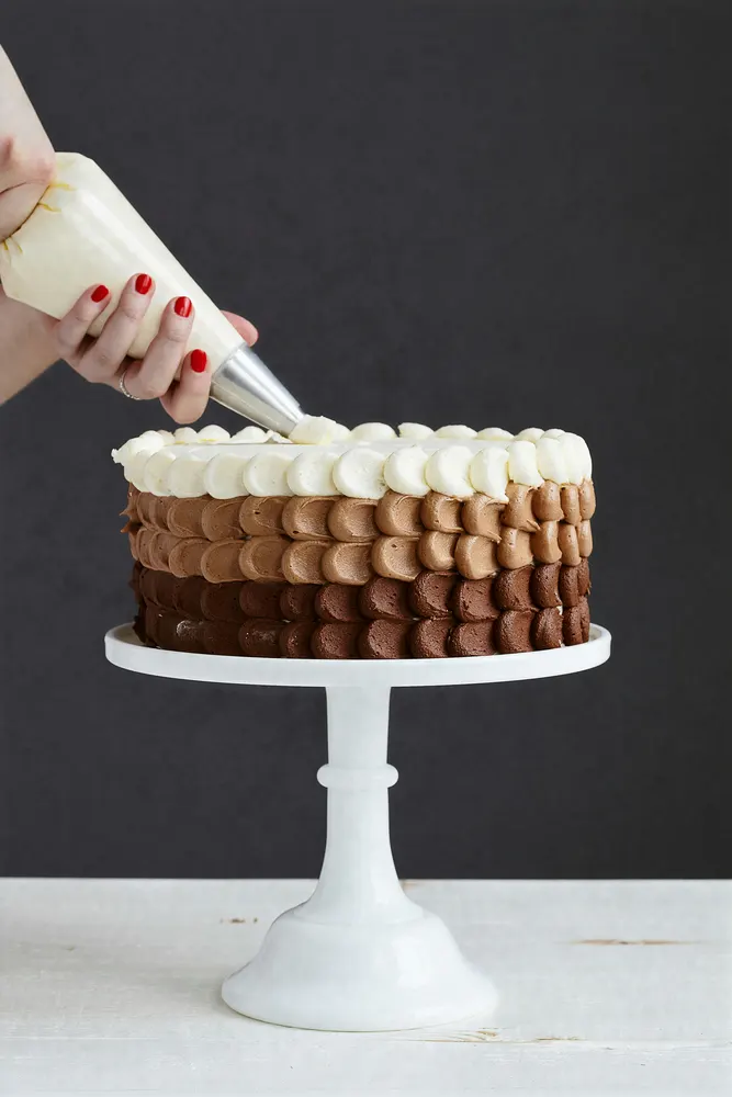 Piping chocolate buttercream rosettes onto a layered cake